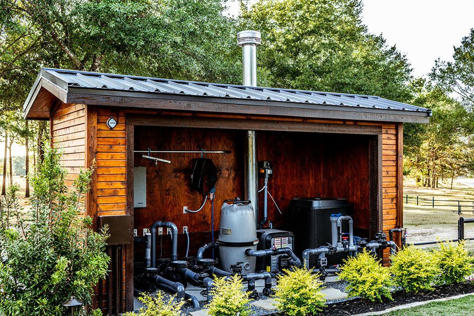 Wooden pool equipment shed with machinery and a metal chimney outdoors.