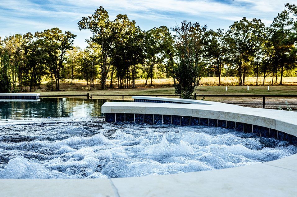 Bubbling spa overlooking a pool, with trees and a blue sky in the background.