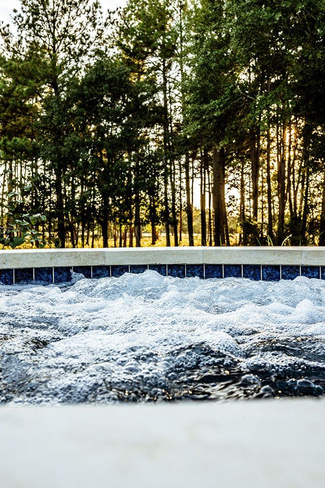 Bubbling hot tub with blue tile trim, forest backdrop and golden sunlight.