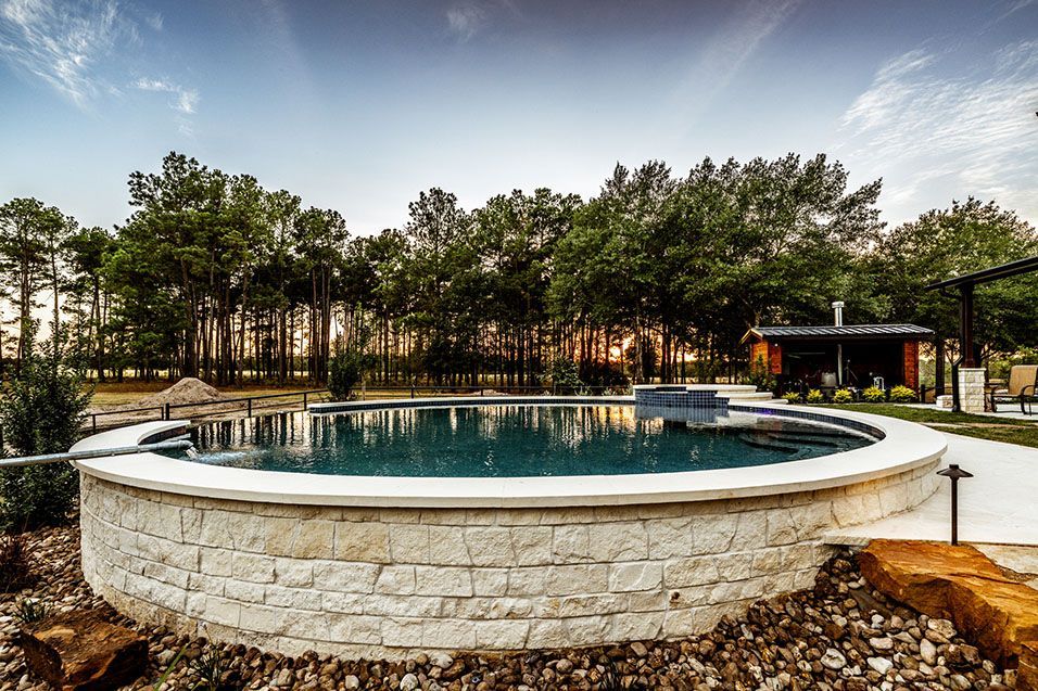 Circular pool with stone border, trees in the background, set at sunset.