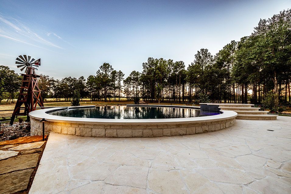 A circular pool with stone surround, windmill, trees in a natural setting.