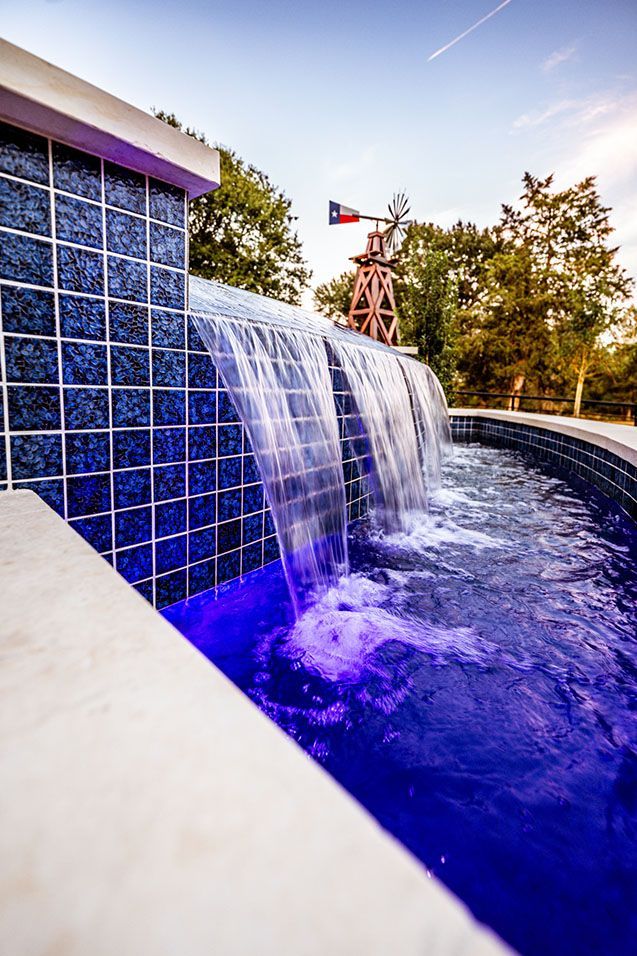 Waterfall feature with blue tile, illuminated water, and Texas flag windmill in the background.