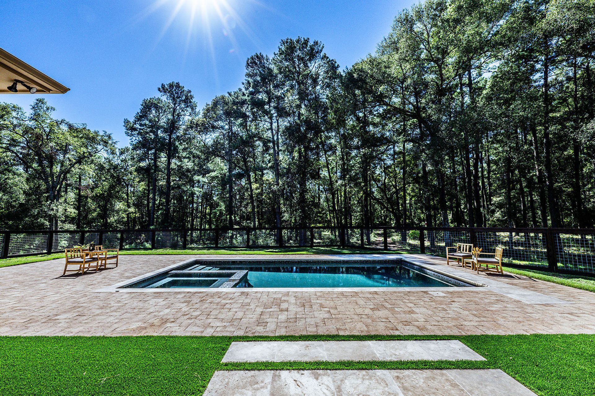 Pool surrounded by sand and grass, with trees in the background under a sunny sky.