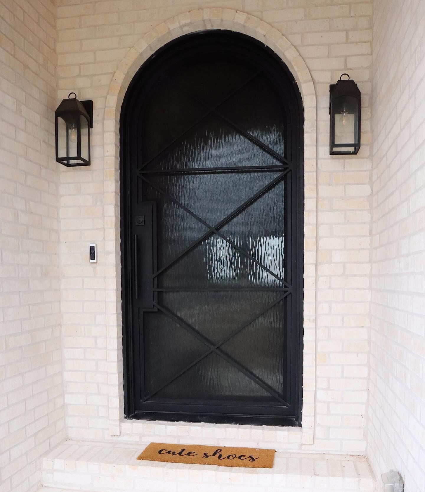 A white brick building with a black door and a welcome mat