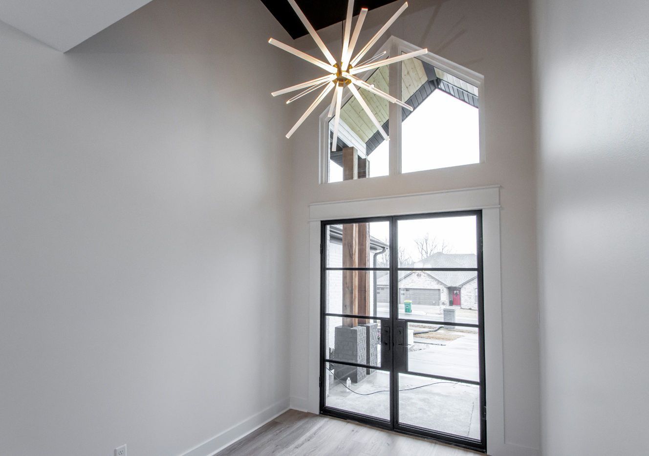 An empty room with a large window and a chandelier hanging from the ceiling.