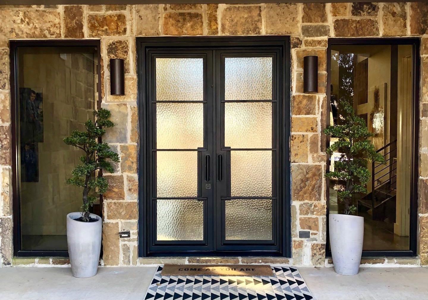 A brick building with a black door and two potted plants in front of it.