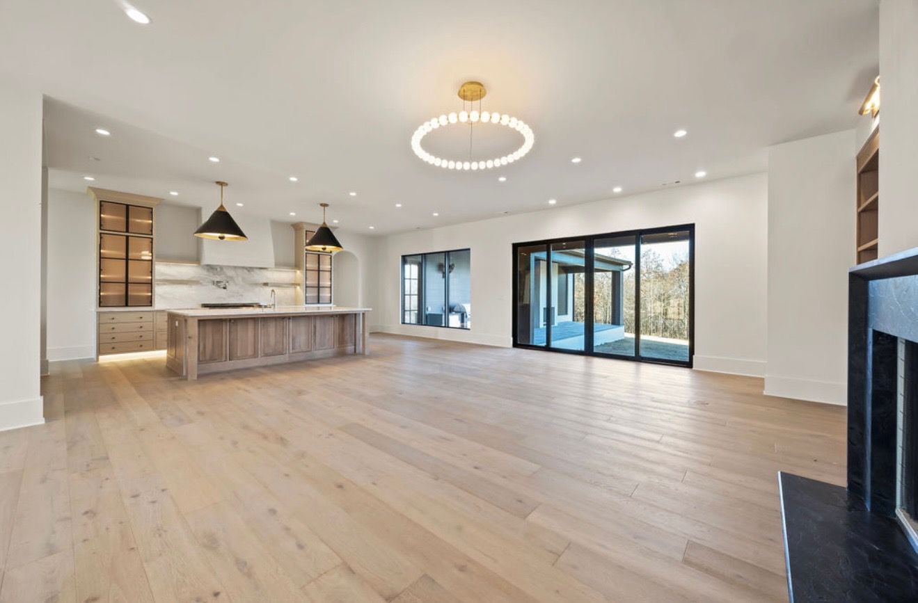 A large empty living room with hardwood floors and sliding glass doors leading to a kitchen.