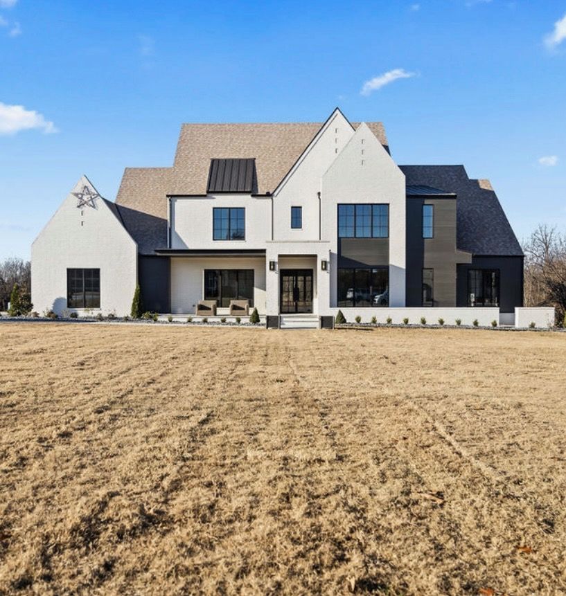 A large white house sits in the middle of a dry field