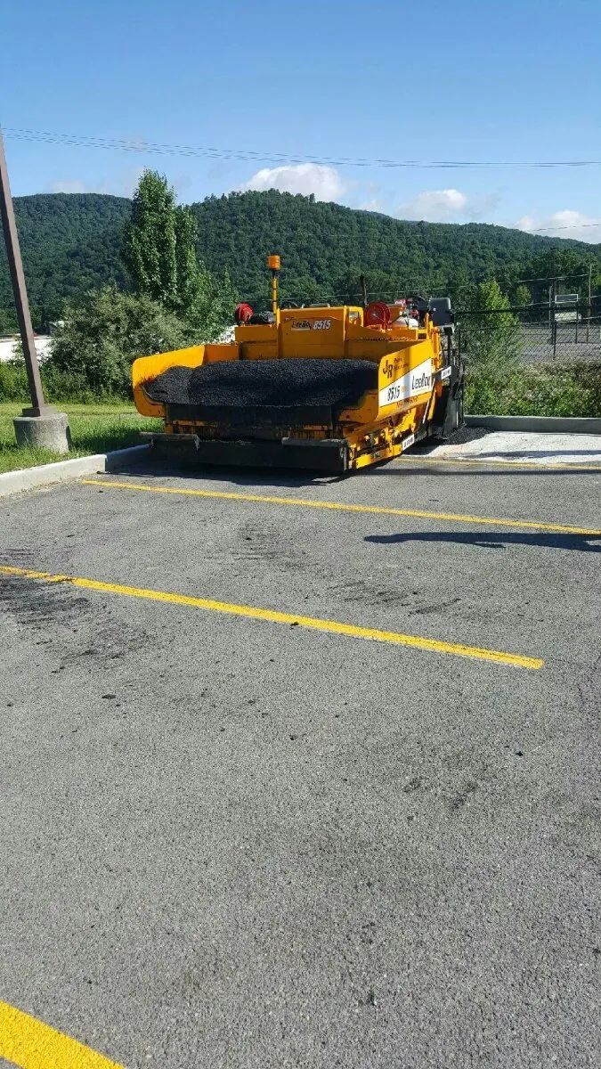 Yellow asphalt paving machine on a parking lot, mountains in background.