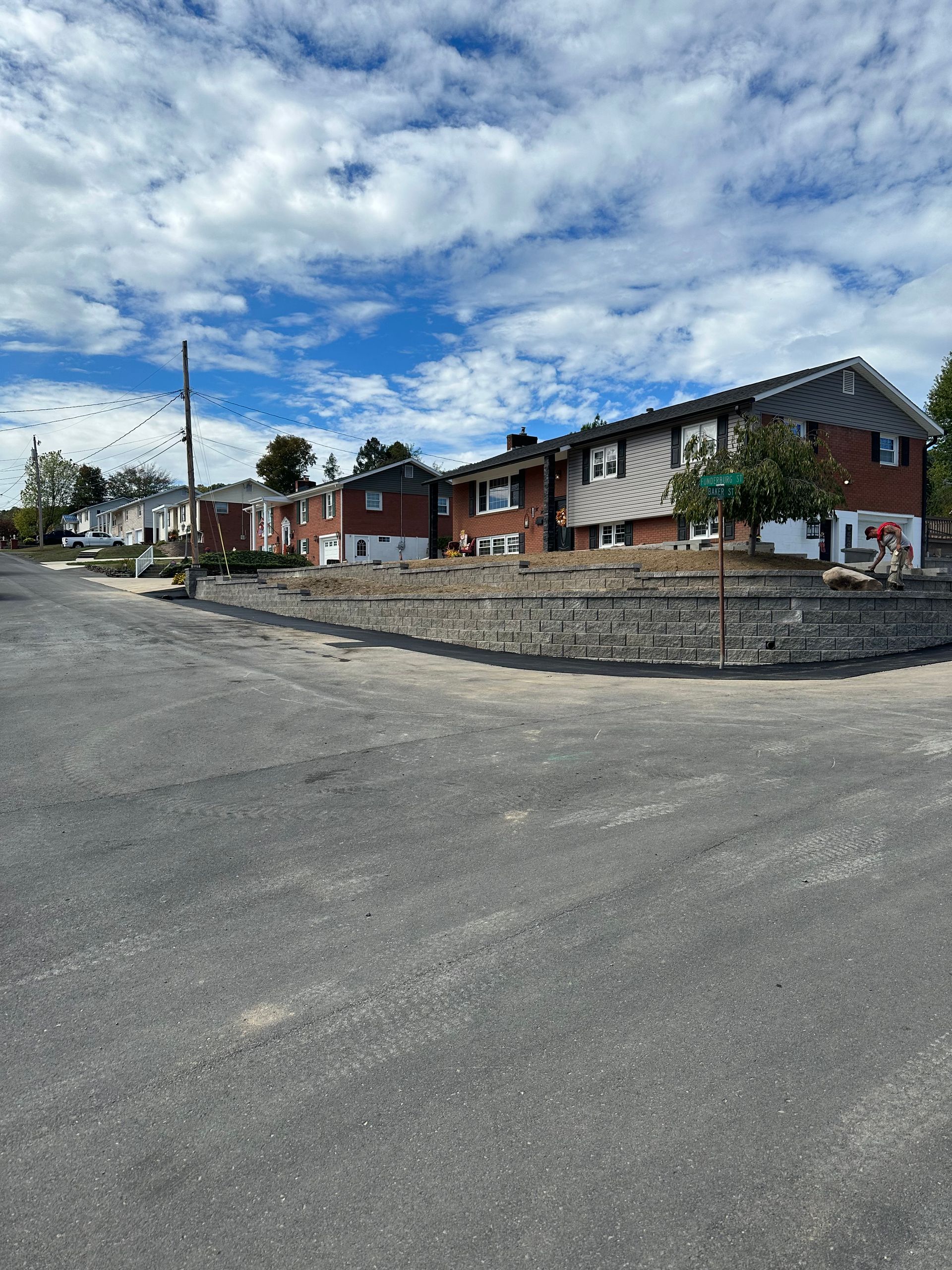 Street view with brick buildings and retaining wall under a cloudy sky.