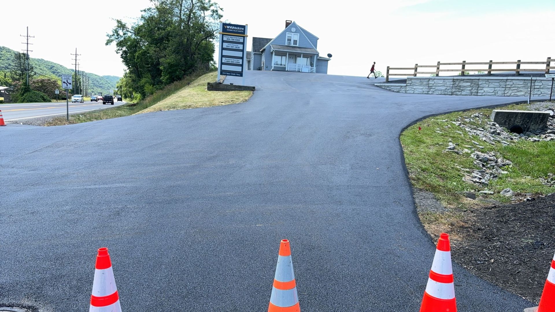 Gravel driveway leading to a building with a sign, edged by orange traffic cones.