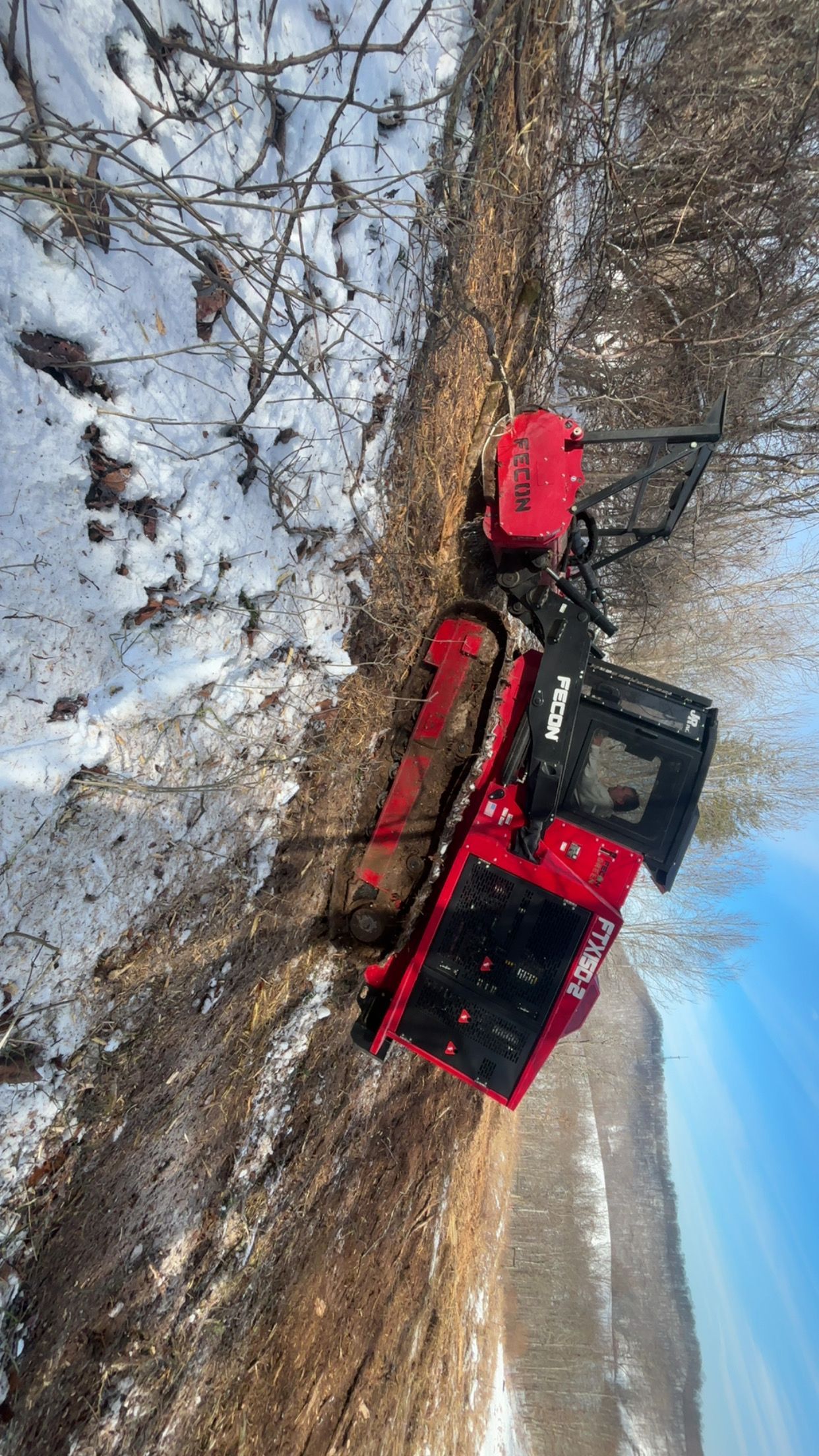 Red utility vehicle on a snowy path next to a line of leafless bushes.