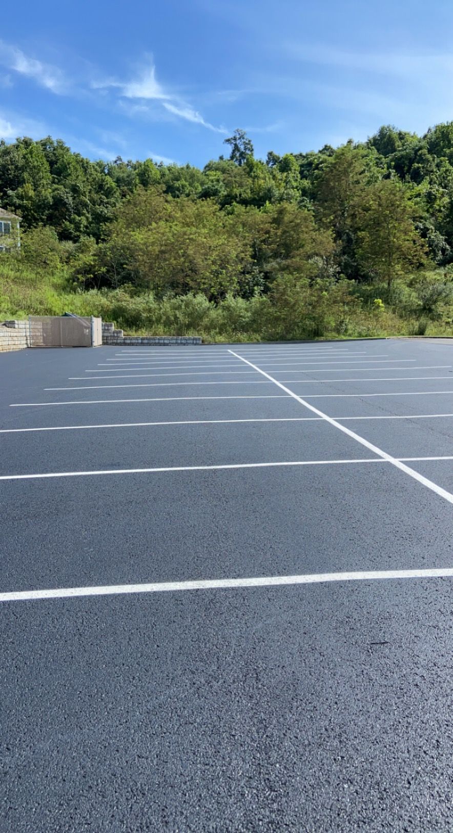 Empty, freshly paved parking lot with white lines, blue sky, and green hillside.
