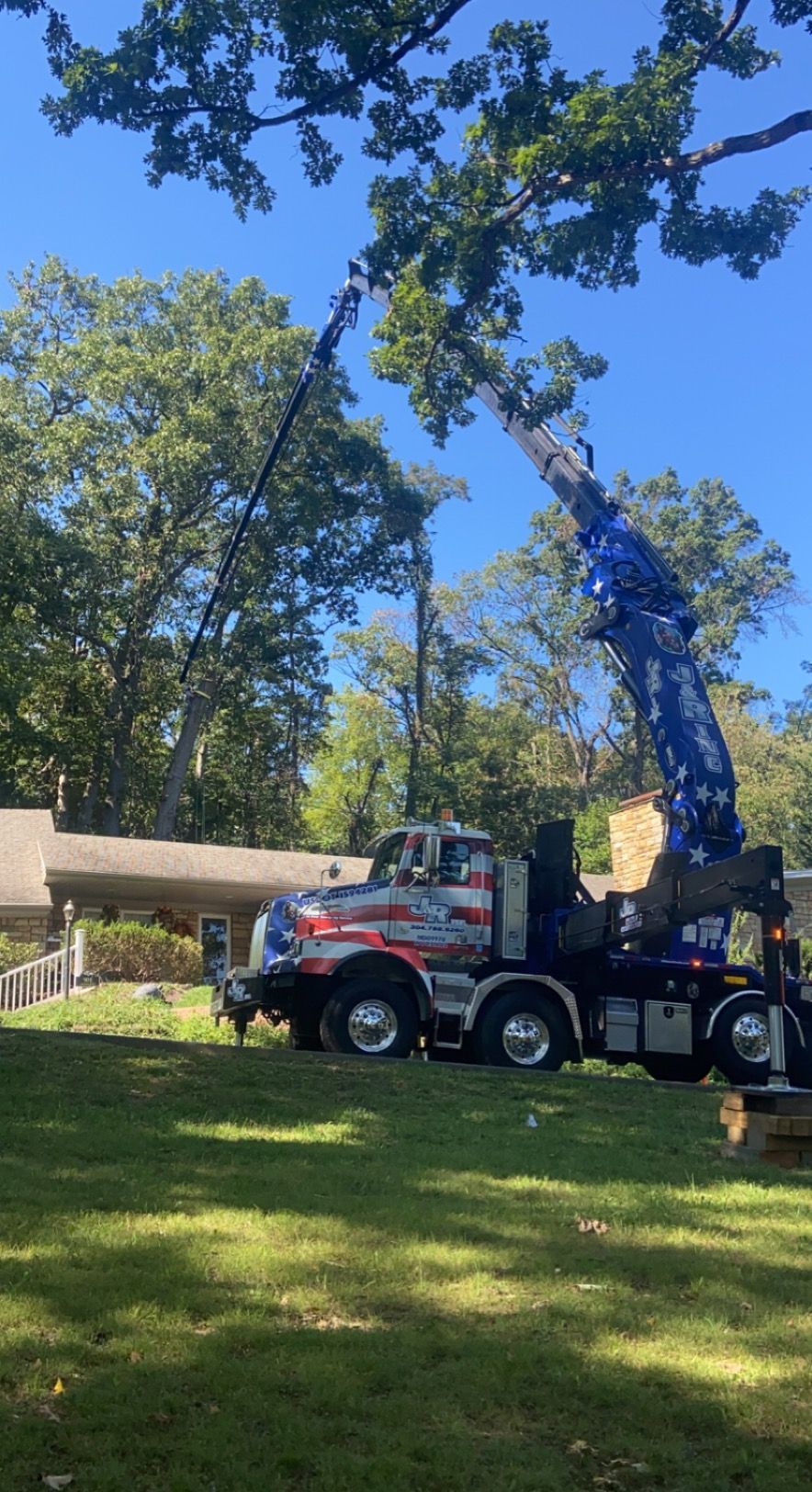 A tree service truck trims a tree in front of a house on a sunny day.