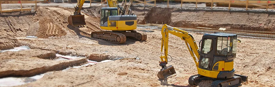 Two yellow excavators are digging in a sandy construction site.