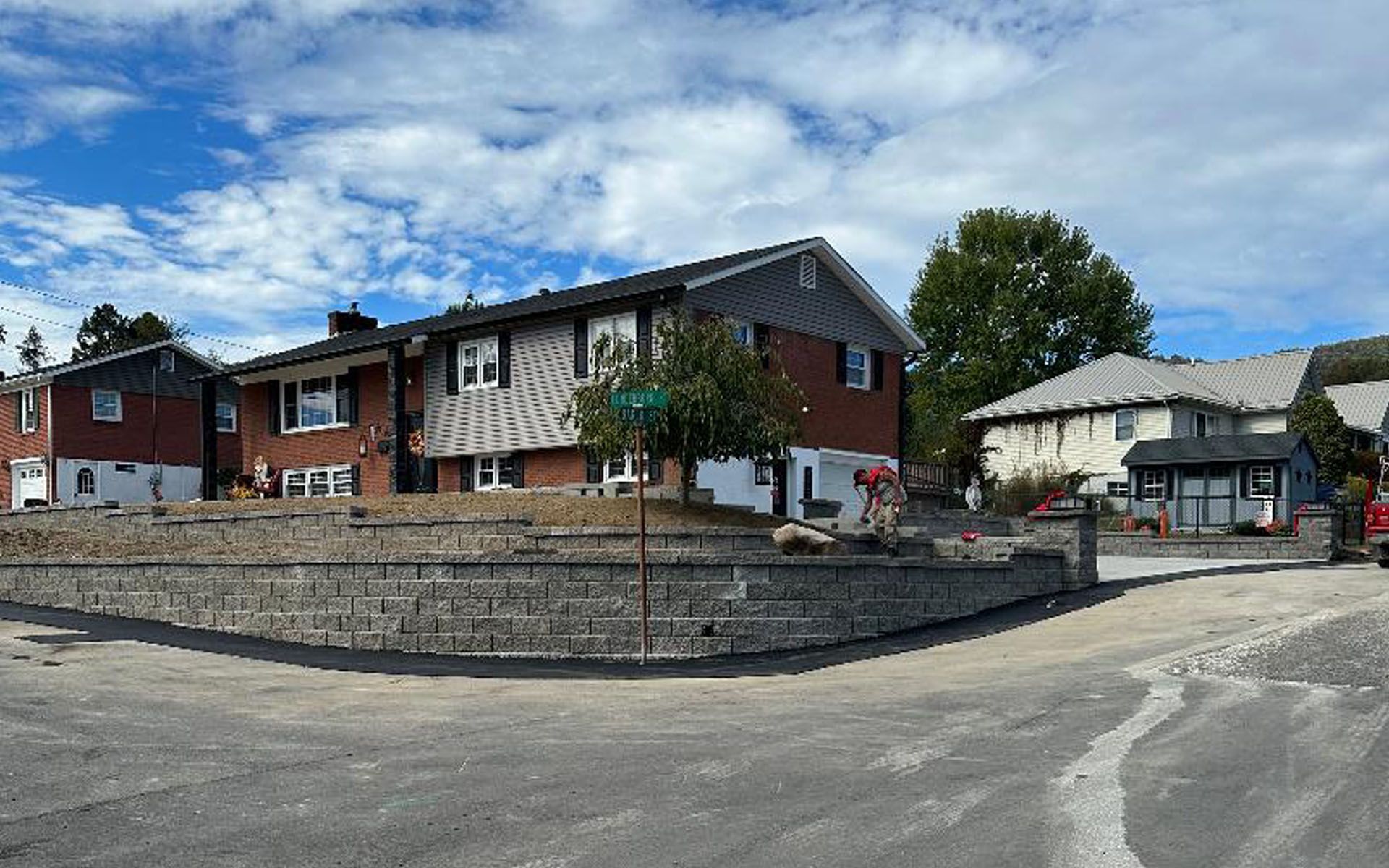 A brick house with a new stone retaining wall on a corner lot, under a blue sky with scattered clouds.