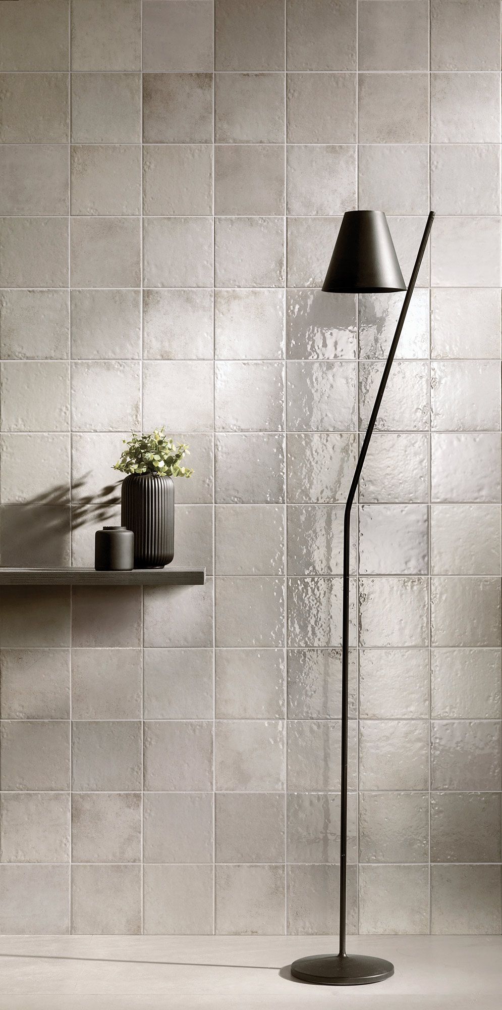 Gray tiled wall with black floor lamp, shelf with vase and candle.