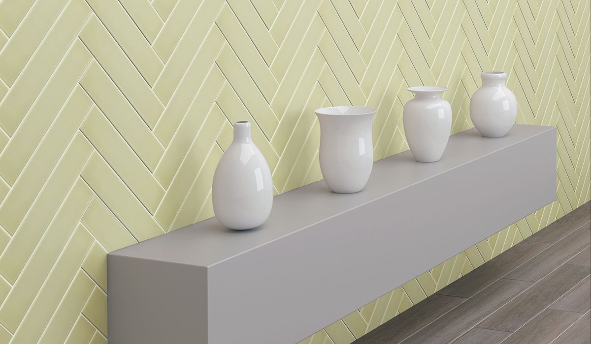 Four white vases on a gray shelf against a yellow herringbone tile wall.