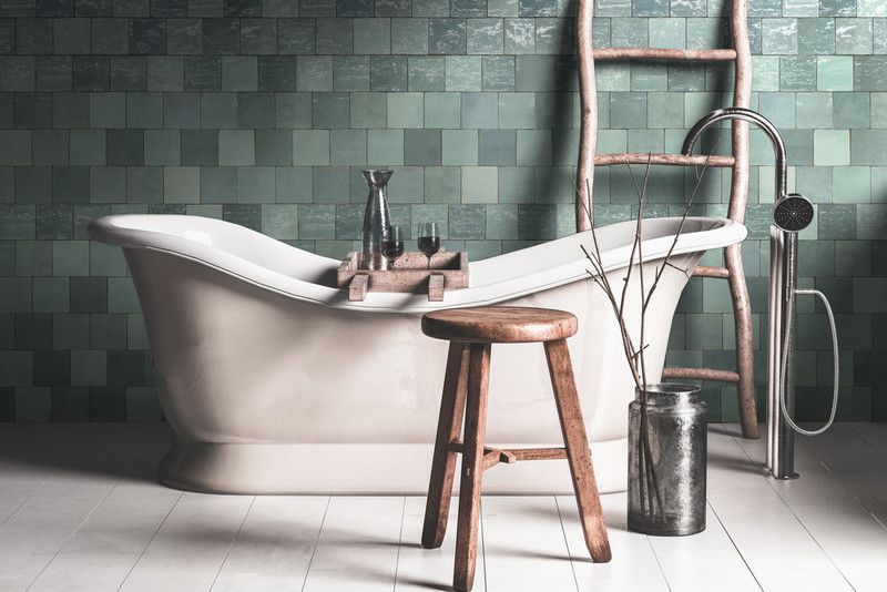 A vintage bathtub in a teal-tiled bathroom, with a wooden stool and ladder.