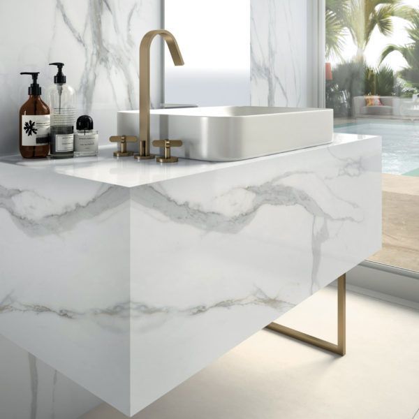 Marble bathroom vanity with gold fixtures, a white rectangular sink, and toiletries.