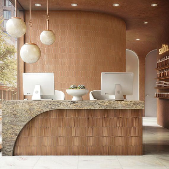 Reception desk with computers and curved wood paneling in a spa with tan walls and hanging globe lights.