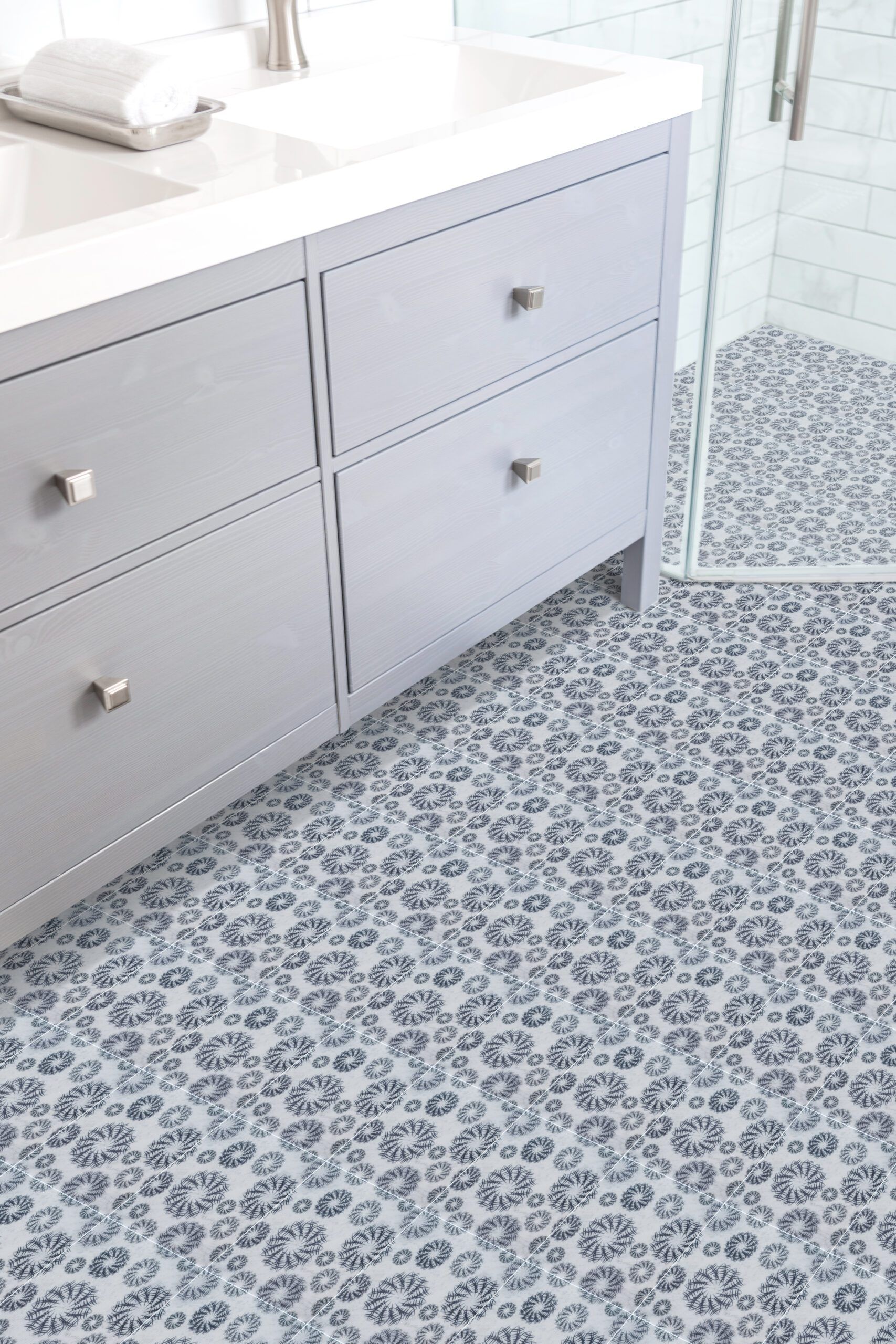 Light blue bathroom floor with a circular pattern. Gray vanity with silver knobs and a shower.