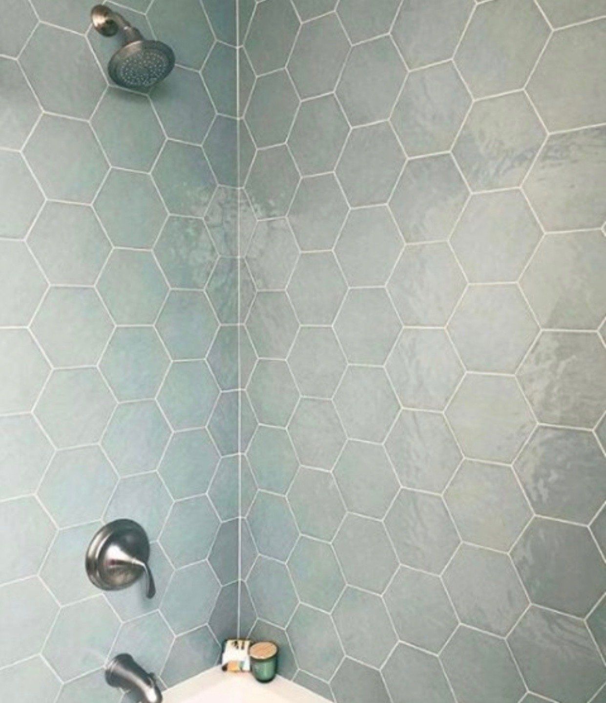 Light blue hexagonal tiles in a shower. Chrome fixtures, white grout. Corner view.