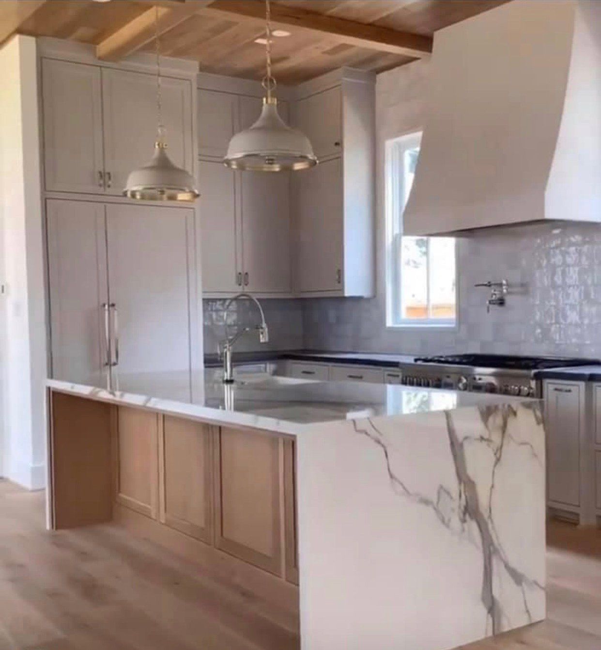 Kitchen with light-colored cabinets, marble countertops, wood ceiling, and gold pendant lights.