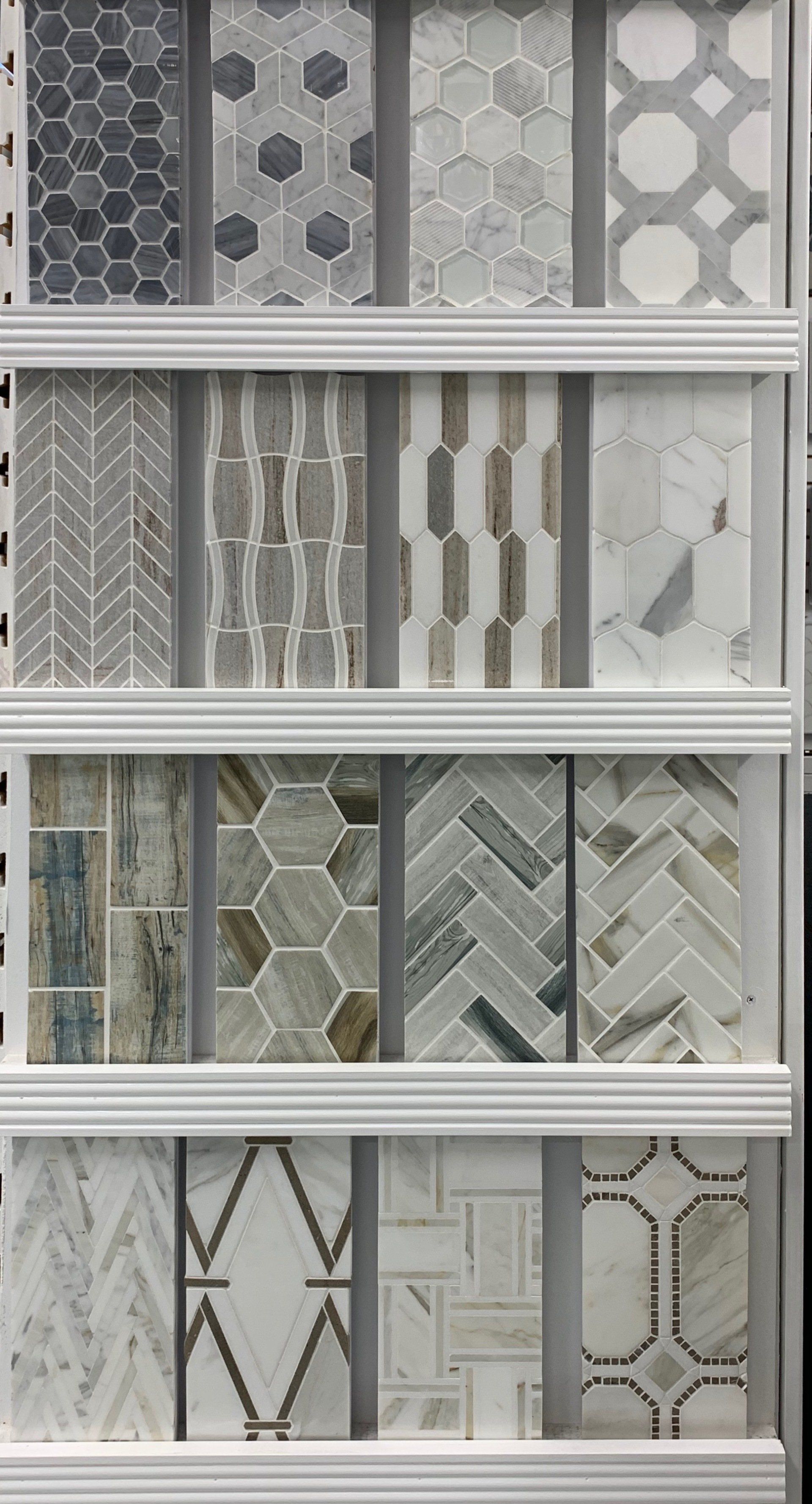 Tile samples arranged vertically on a white display rack, showcasing various mosaic patterns and colors.