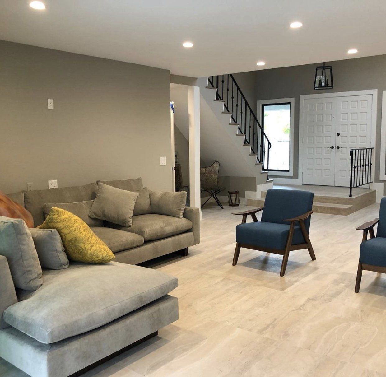 Living room with gray couch, blue armchairs, stairs, and white double doors.