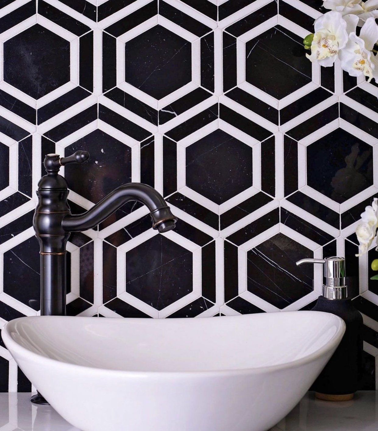 Black and white geometric tiled wall, with a black faucet, white sink, and soap dispenser.