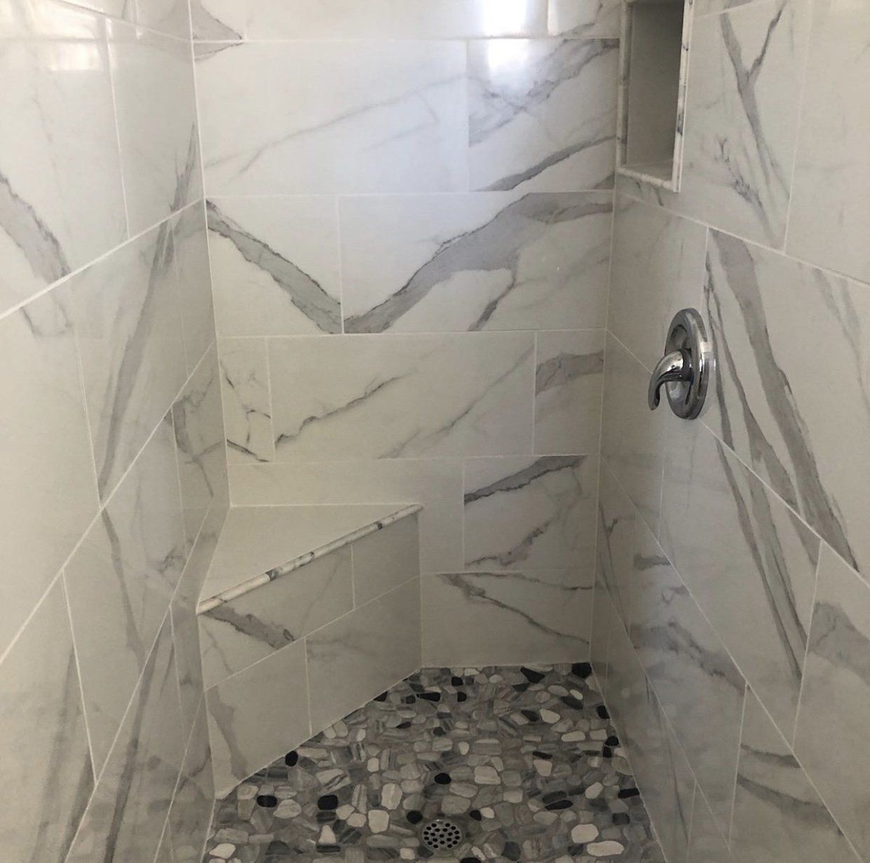 Marble-tiled shower with pebble floor and built-in bench. Silver shower fixtures.