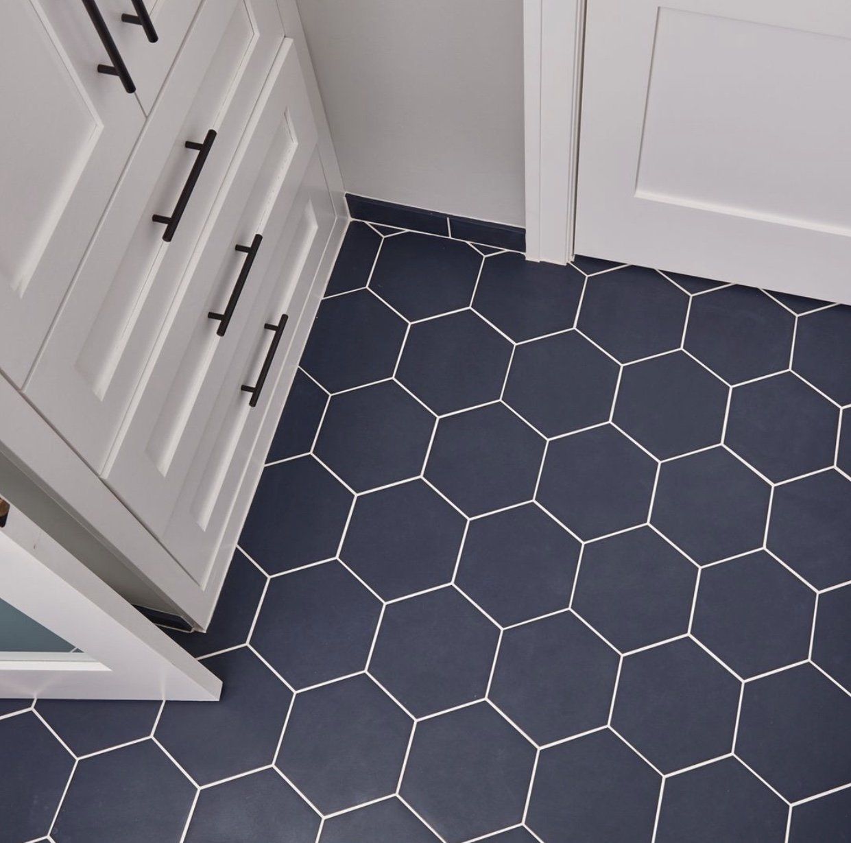 Dark blue hexagon tile floor between white cabinets.