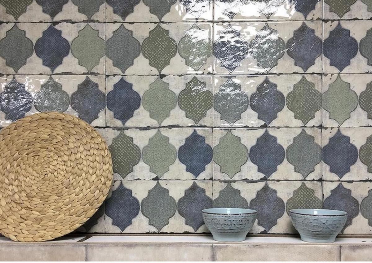 Woven mat and two blue bowls on a shelf below patterned blue and green tiles.