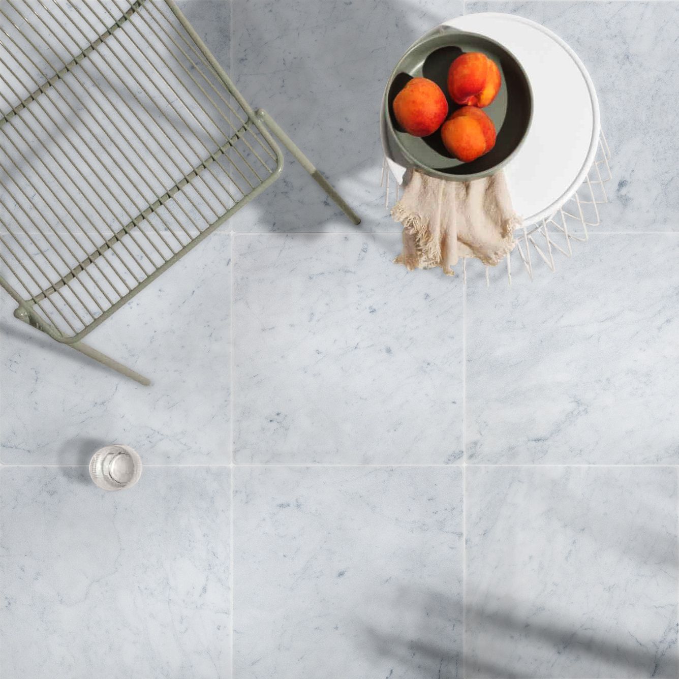 Overhead view of a patio with marble tile. A metal chair, small table with peaches, and a glass are present.