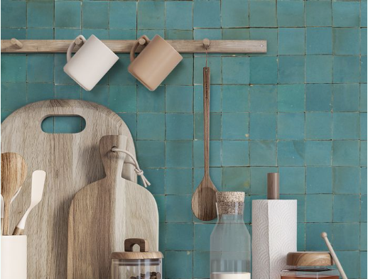 Kitchen counter with teal tile backsplash, wooden cutting boards, mugs, and utensils.
