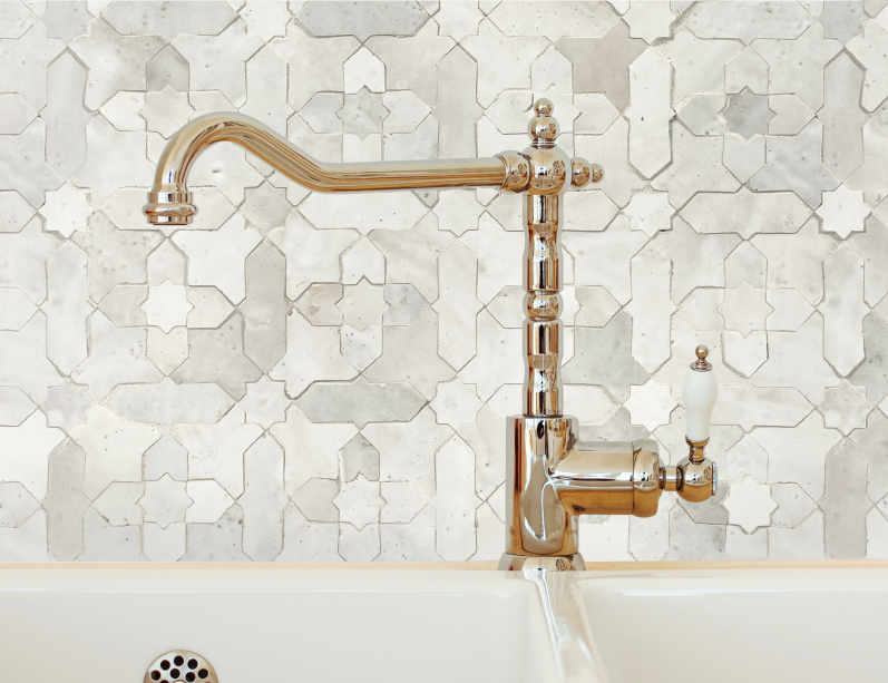 Shiny faucet pouring water into a white sink against a geometric patterned tile wall.