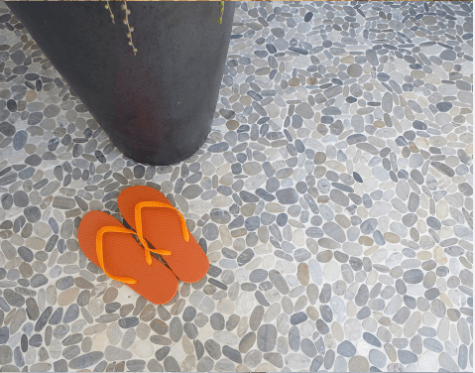 Orange flip-flops on pebbled floor near a black pot.
