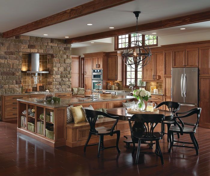 Rustic kitchen with wood cabinets, stone wall, and large island with bench seating and dining table.