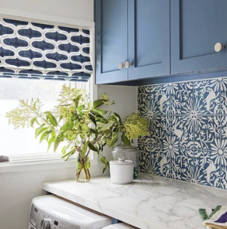 Laundry room with blue cabinets, patterned tile backsplash, and window with patterned shade.