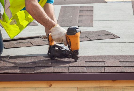Worker using a nail gun to install shingles on a roof