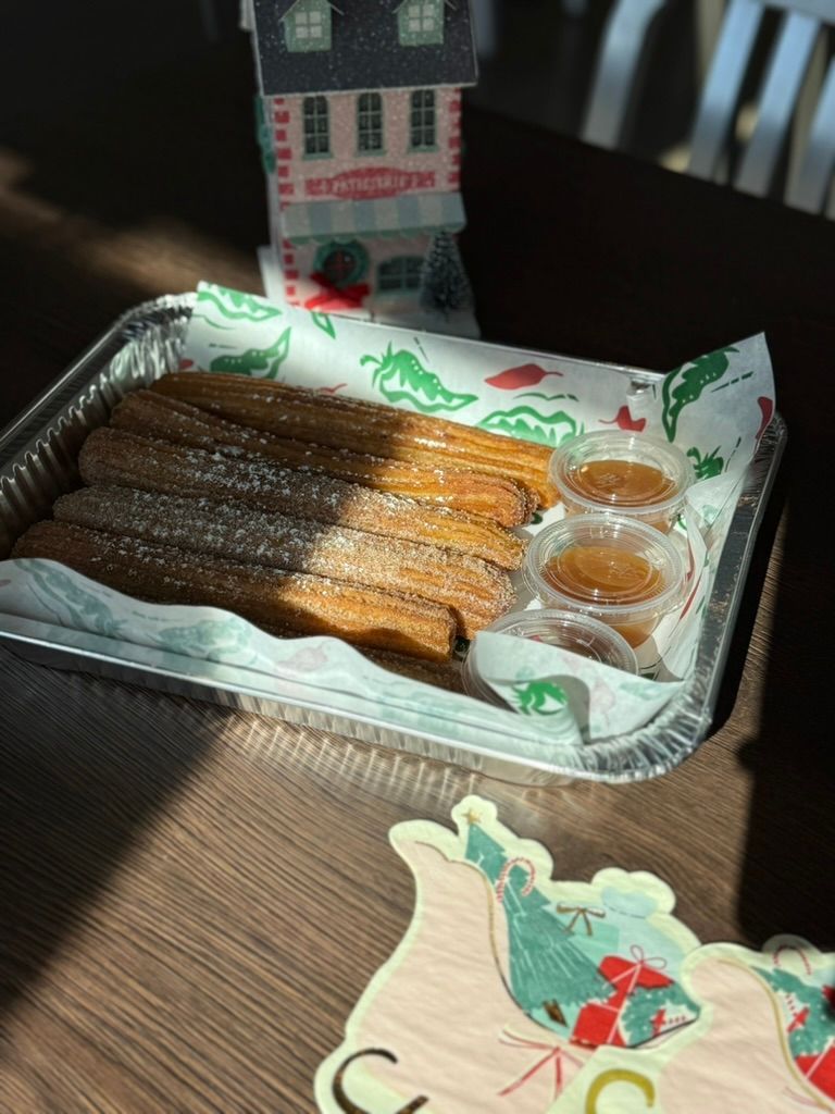Tray of churros with dipping sauces on a table, with a small decorative house in the background.