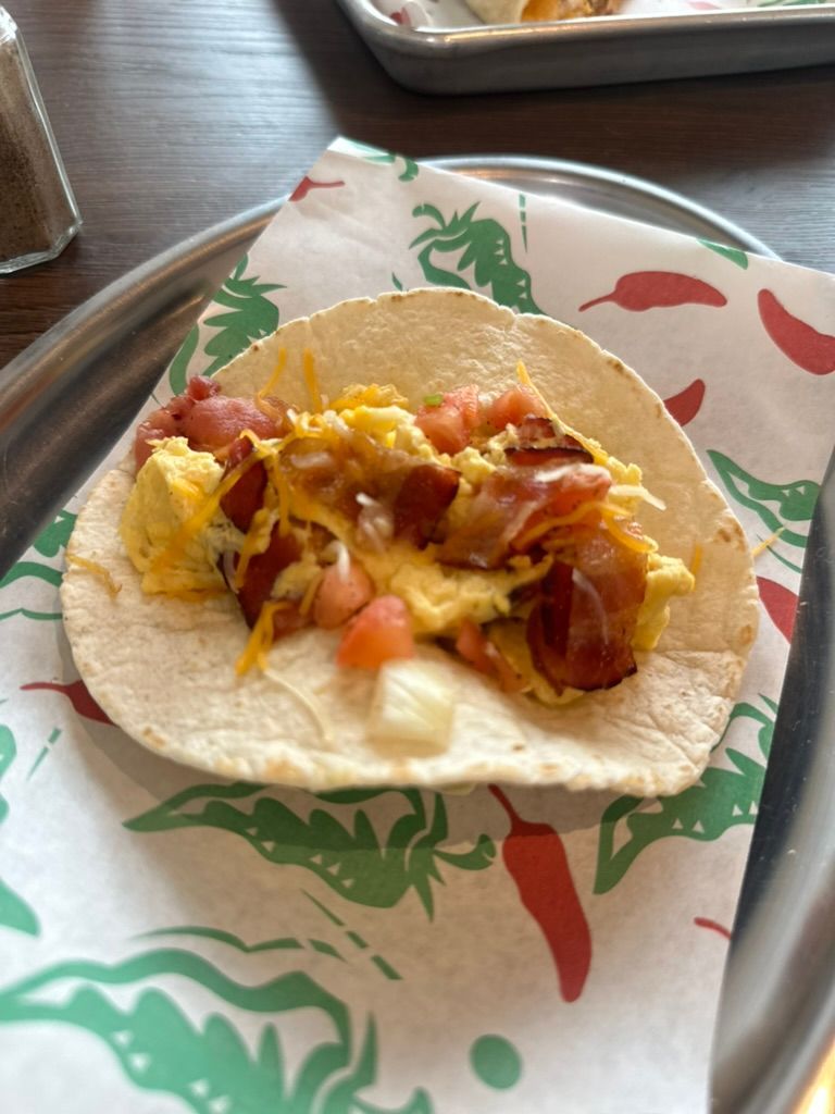 Tortilla taco on a paper-lined tray, topped with melted cheese, meat, and diced tomatoes.