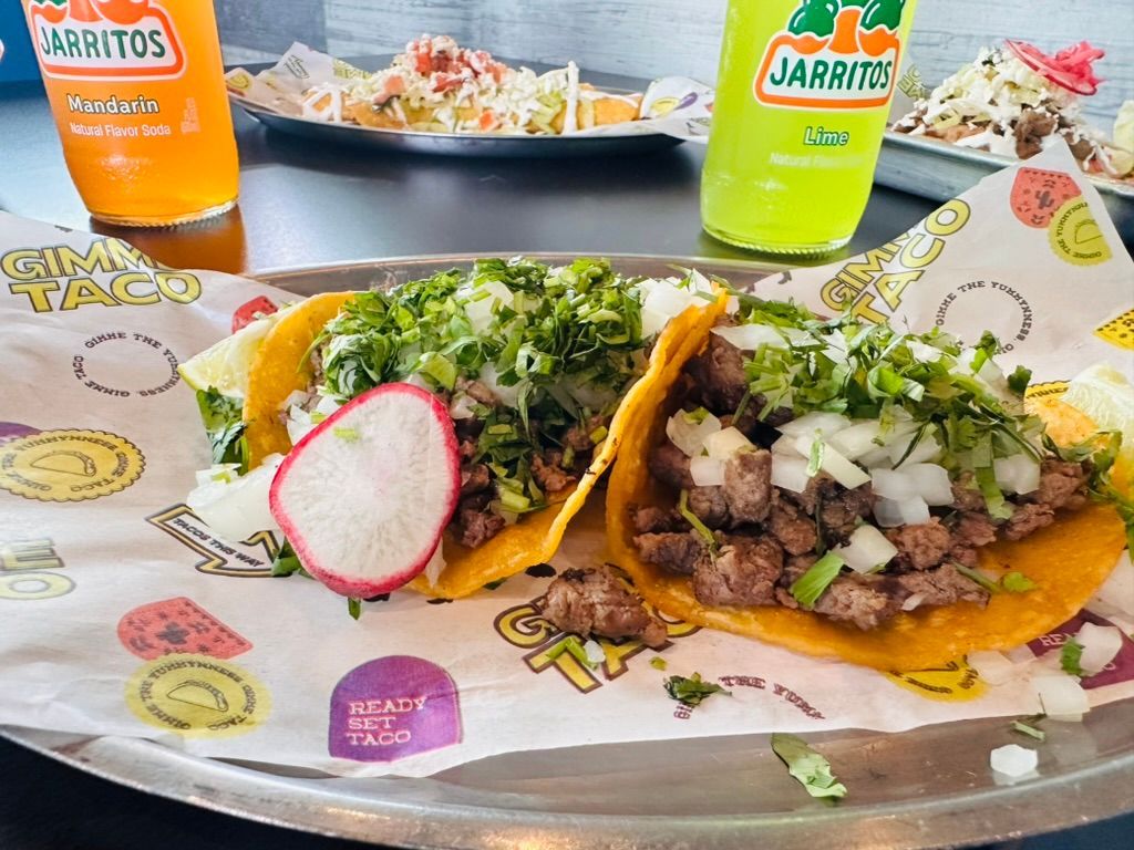 Taco meal on branded tray with two tacos, radish, and drinks on a restaurant table