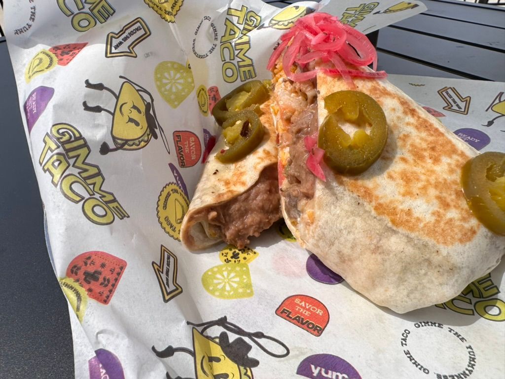 Close-up of a burrito with green olives and pink pickled onions on printed food paper.