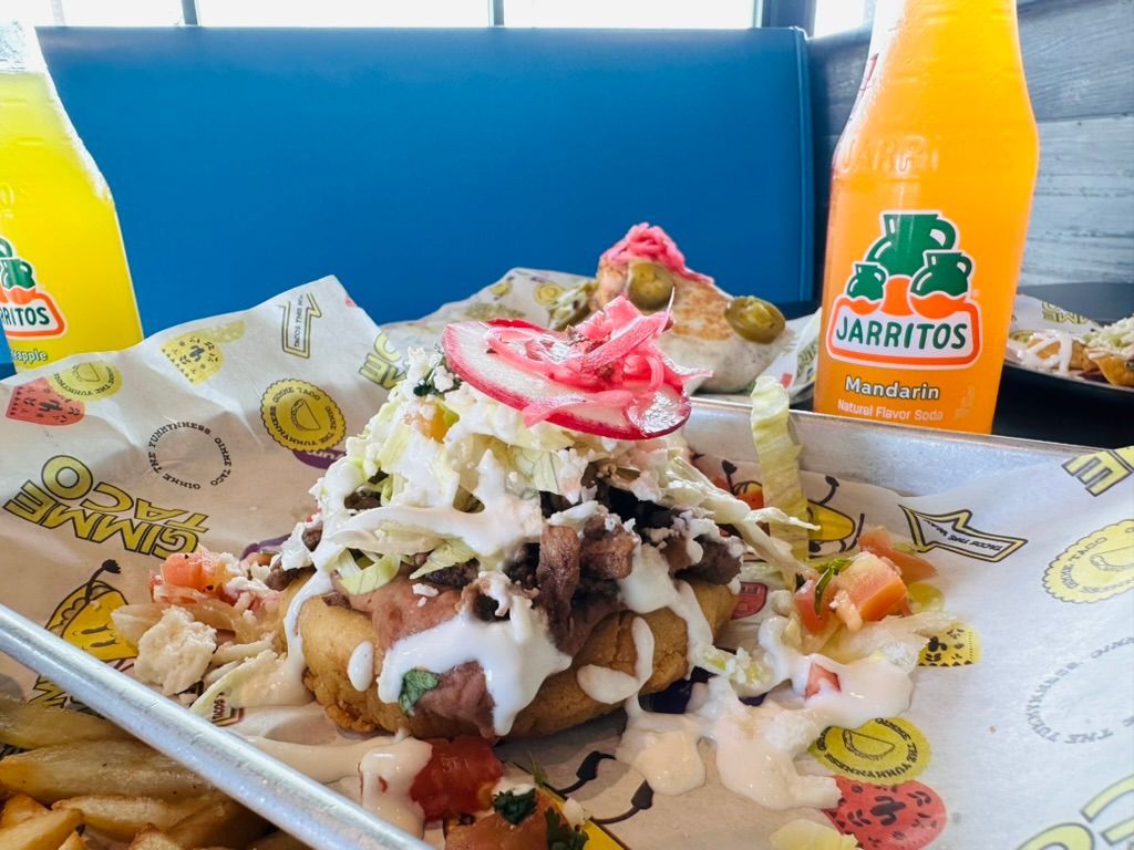 Loaded nacho platter with toppings and sauces, flanked by two orange Jarritos drinks on a table.