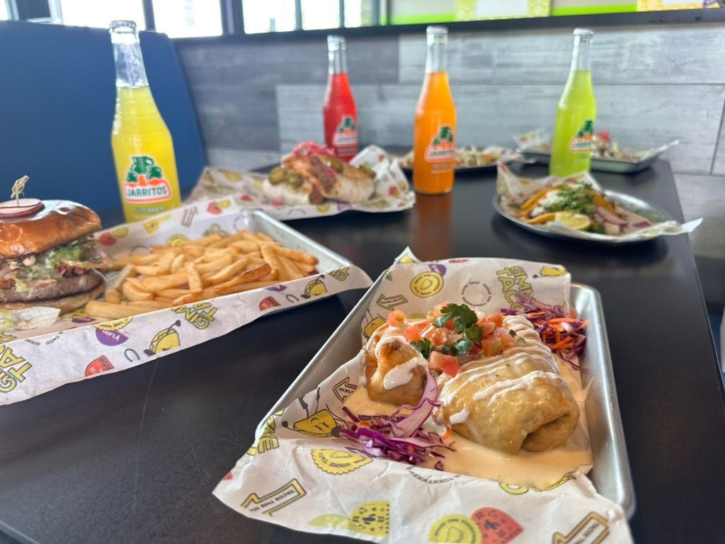 Assorted plated meals and colorful drinks on a table by a window, with fries and sandwiches visible