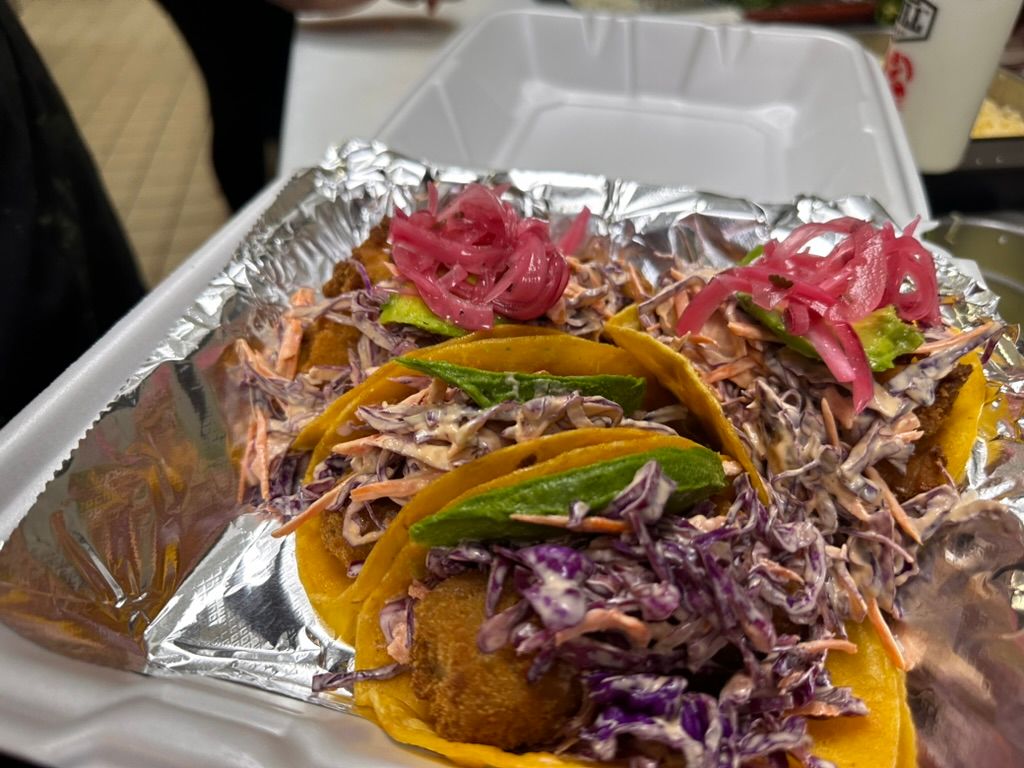 Foil tray of tacos topped with purple cabbage, pickled onions, and green peppers on a table