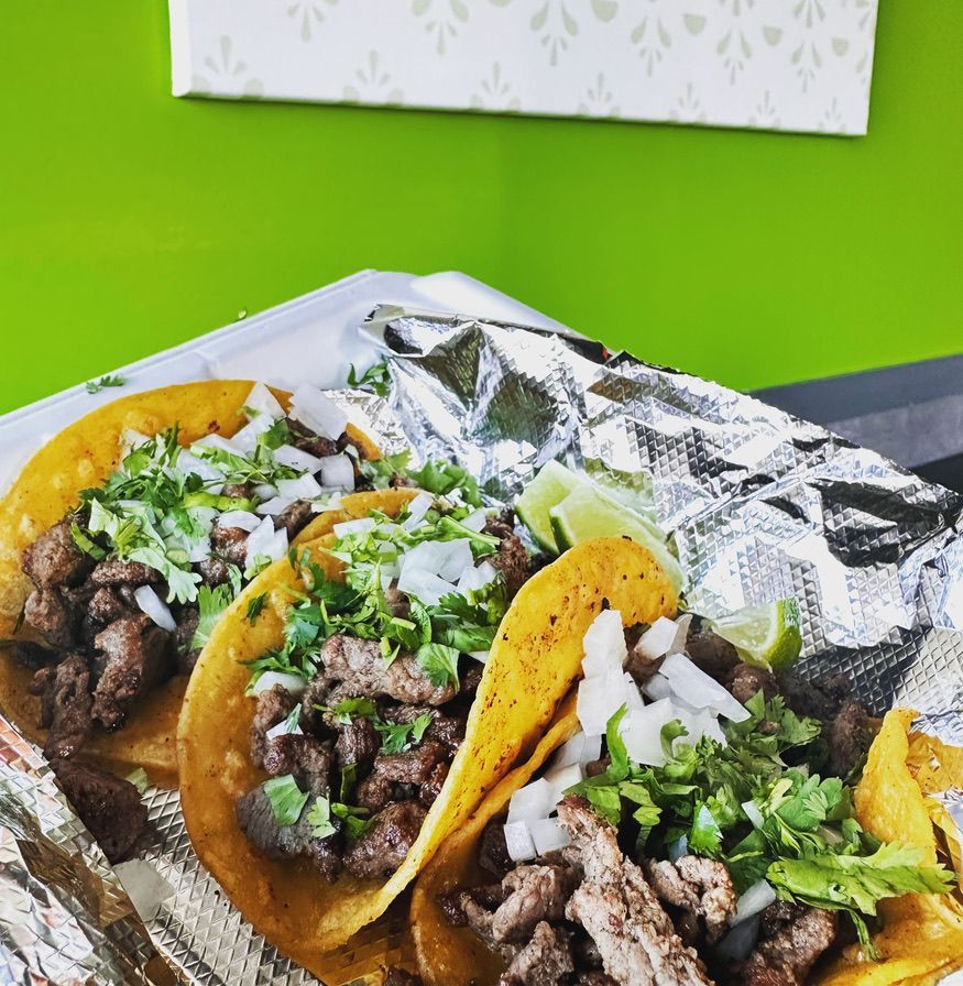 Tacos with grilled meat, cilantro, and onions on foil, against a bright green background