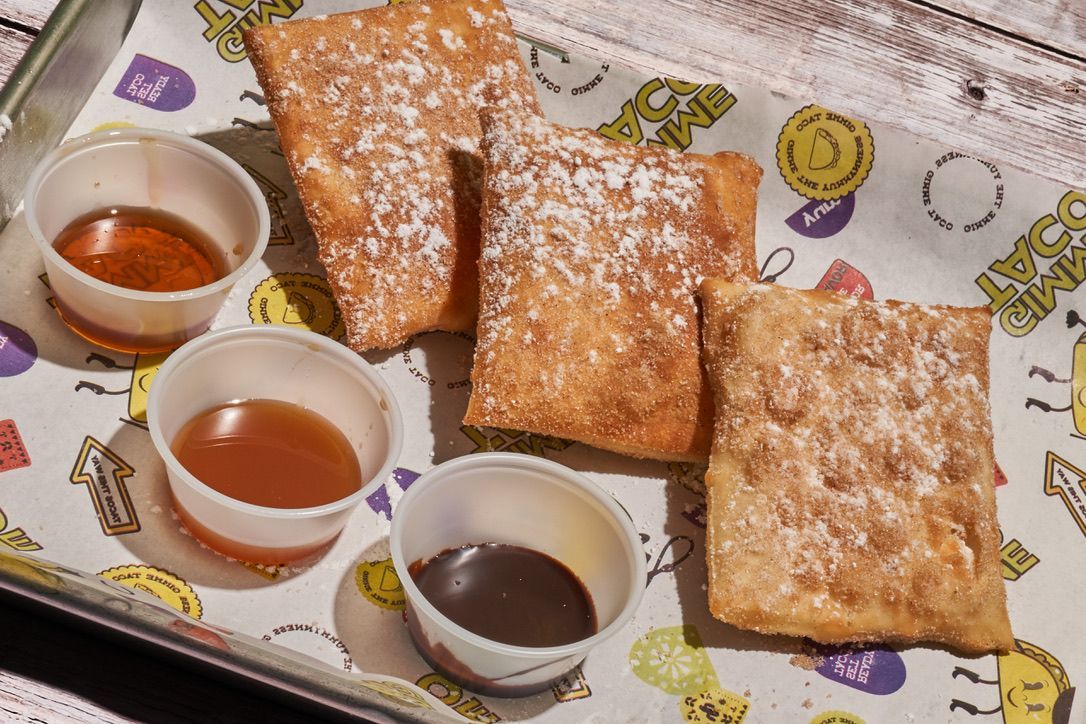 Tray of powdered pastries with three small dipping sauces on a patterned napkin.